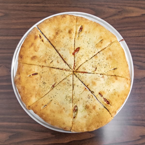 A golden-brown pizza pie, cut into eight slices, on a silver pan atop a wooden table.