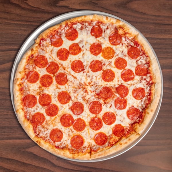 A whole pepperoni pizza, cut into slices, on a metal tray atop a dark wooden table.