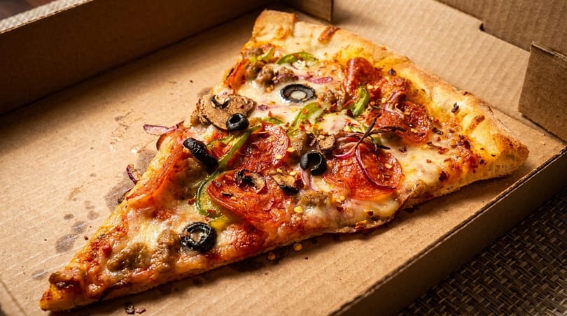 A single slice of pepperoni, olive, mushroom, and pepper pizza in a cardboard delivery box.
