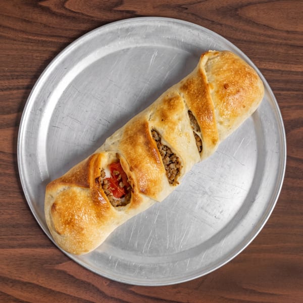 A golden-brown baked pastry filled with ground meat and red peppers on a metal tray.
